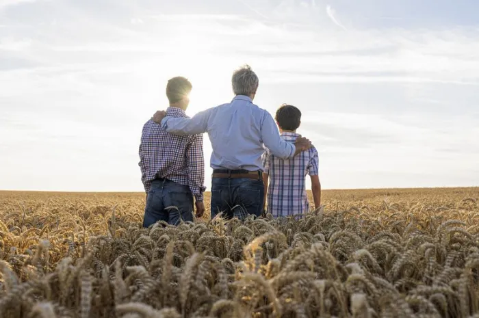 Three generations of farmers standing in a field looking out at the horizon